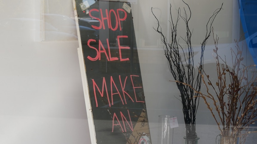 A blackboard with pink writing saying 'shop sale make an offer' inside an empty shop.