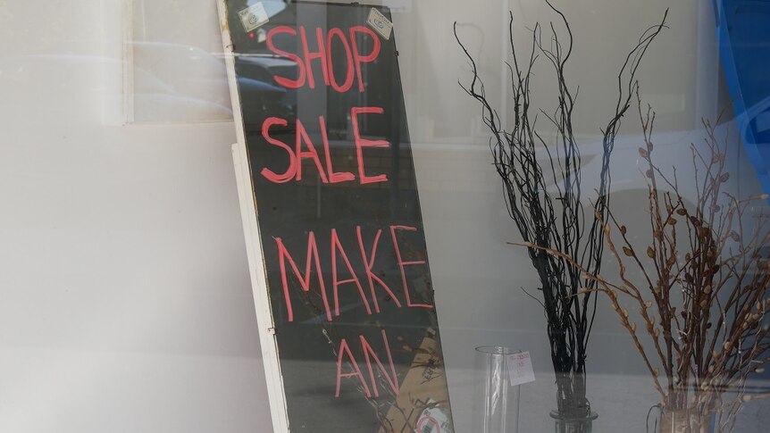 A blackboard with pink writing saying 'shop sale make an offer' inside an empty shop.