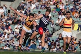 Ed Langdon of the Fremantle Dockers kicks the ball with two Adelaide Crows players in pursuit.