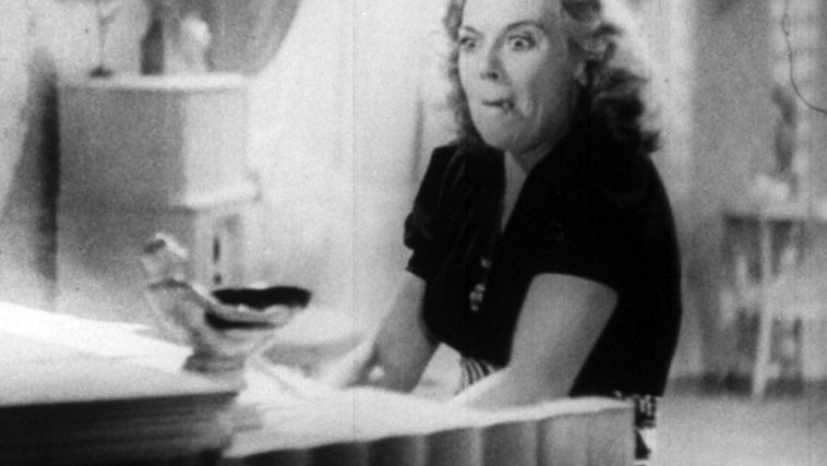 A black and white still of a woman manically playing piano while smoking a joint.