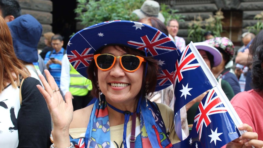 Jamie "from Sydney" grins, wearing an Australian flag hat and holding a small flag.