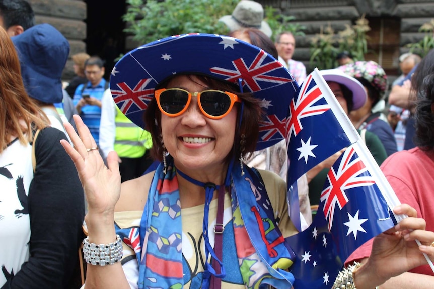 Jamie "from Sydney" grins, wearing an Australian flag hat and holding a small flag.