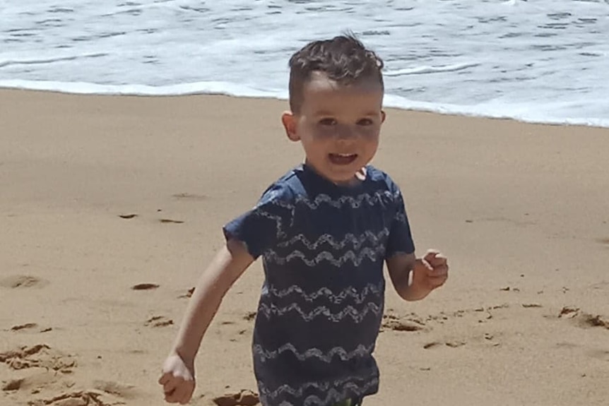 A young boy aged three runs along a beach