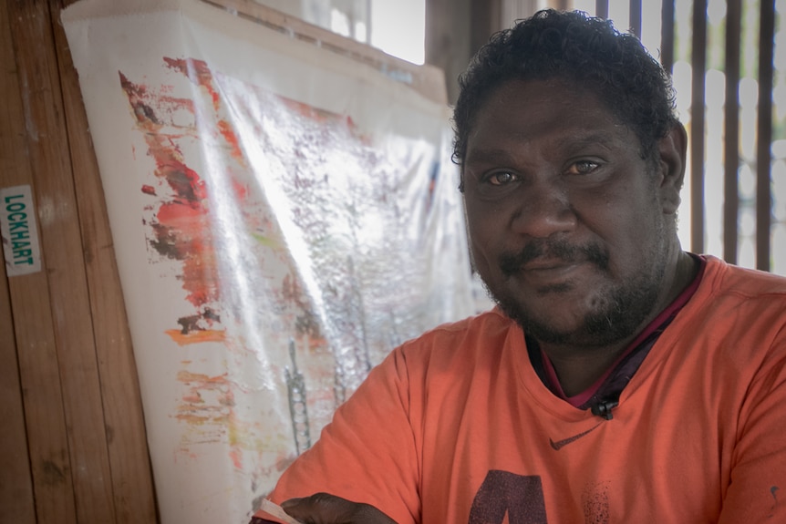 Indigenous artist Silas Hobson stands in front of his canvas.