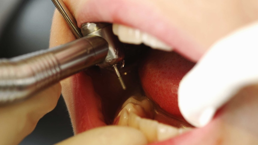 A dentist puts a metal drill inside a child's mouth.