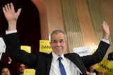 Alexander Van der Bellen holds his hand in the air in front of a crowd.