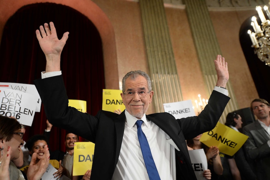 Alexander Van der Bellen holds his hand in the air in front of a crowd.