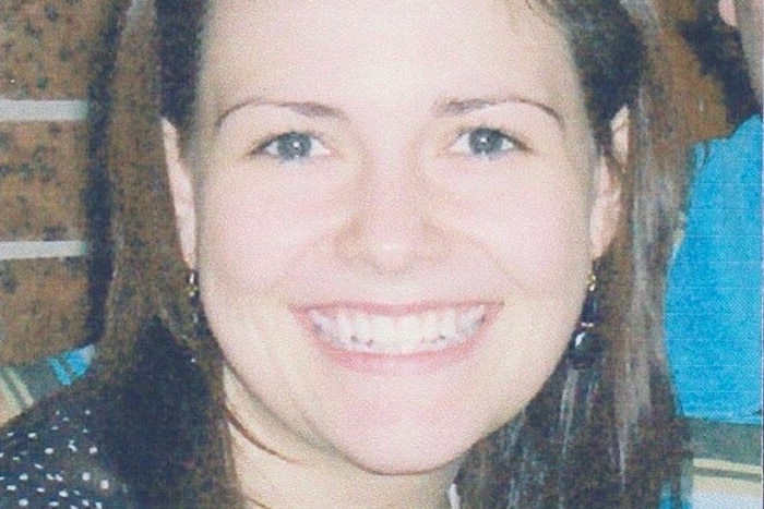 A smiling young woman with sunglasses on her head, photographed in front of a brick wall.