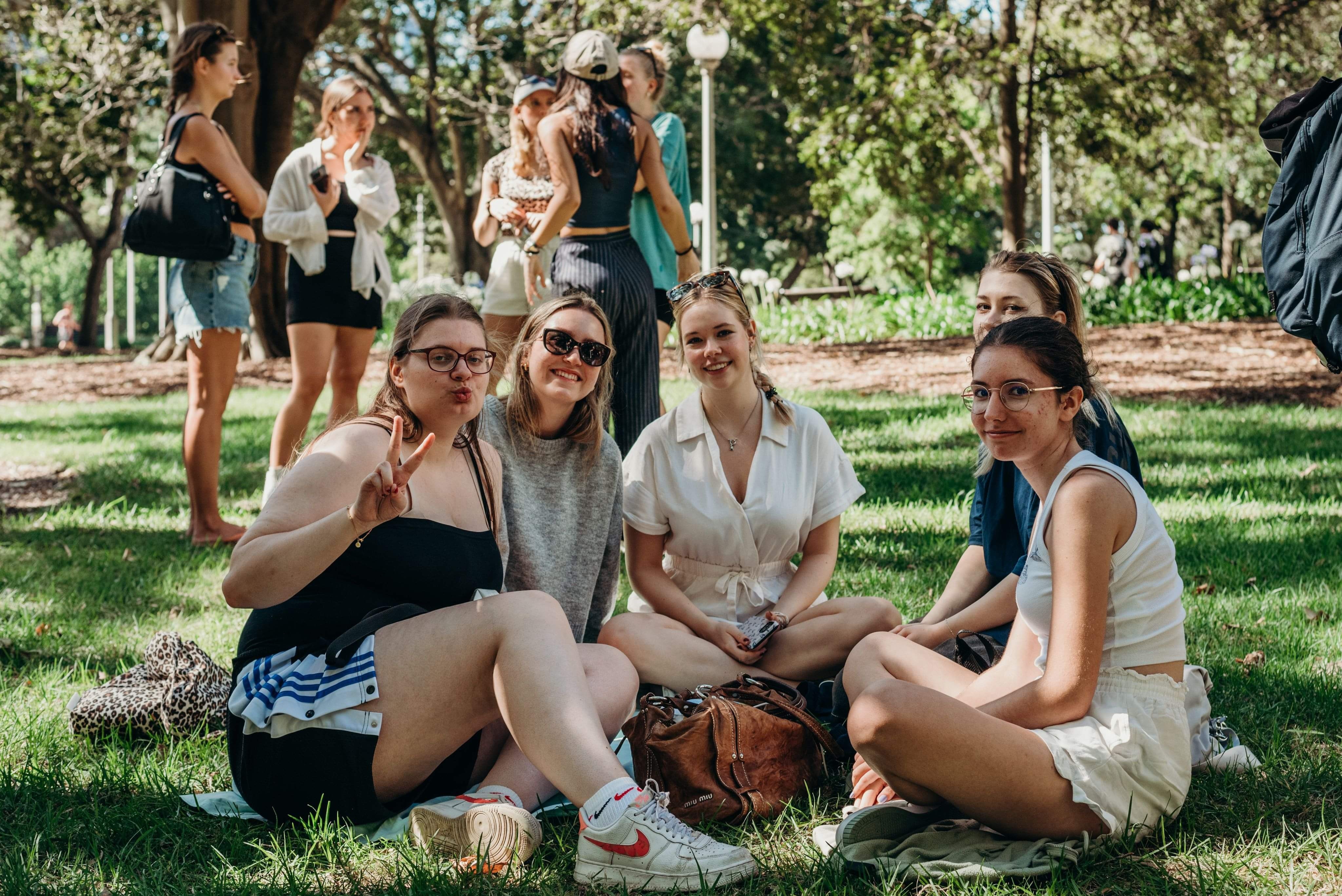 Five women sitting on the grass with four others standing up.