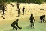 Blurry image of a group of people gathered on the sand and in the shallows of the water on a beach