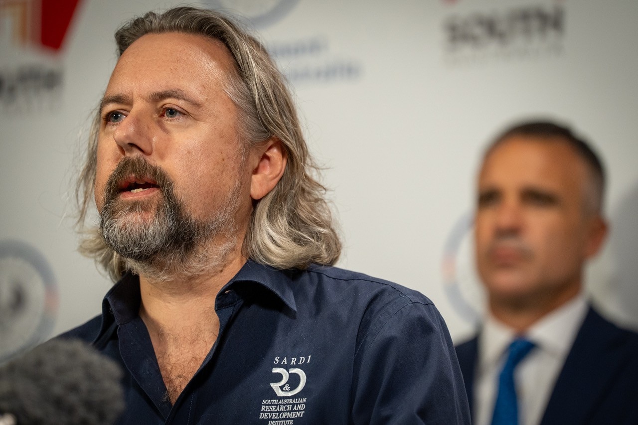 El profesor Mike Steer habla con los medios en primer plano, con el primer ministro Peter Malinauskas al fondo.