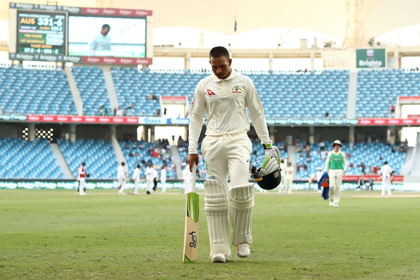 Wide shot of a cricket batsman walking from the field.