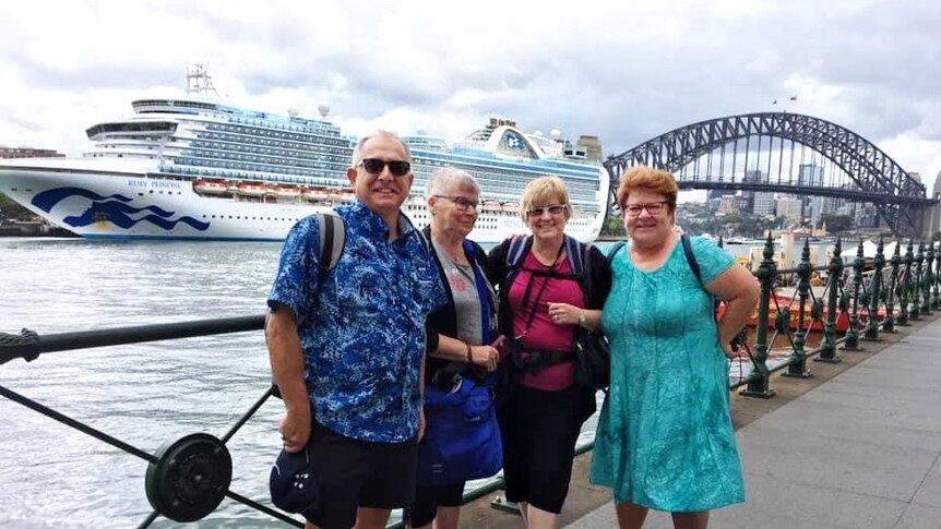 A group of people smiling and happy in the harbour with a cruise ship in the background.