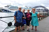 A group of people smiling and happy in the harbour with a cruise ship in the background.