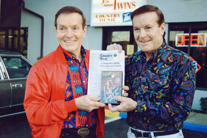 two identical twins hold a newspaper clipping about graeme connors