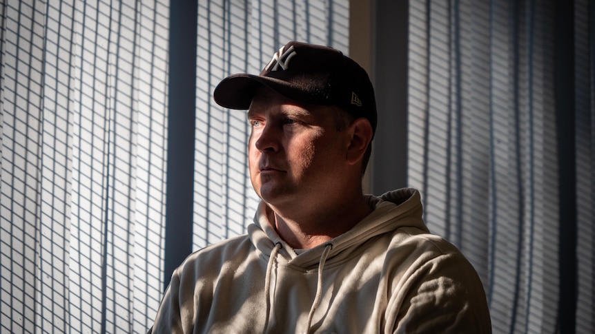 Frank Gallagher indoors with the shadow of blinds over his face, wearing New York Yankees cap.