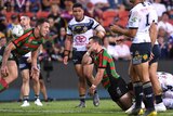 An NRL player flings the ball away in triumph after scoring a try as his teammate looks on.