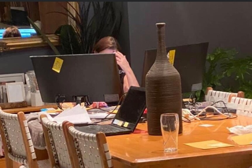 A woman sitting at a table swamped by computer monitors