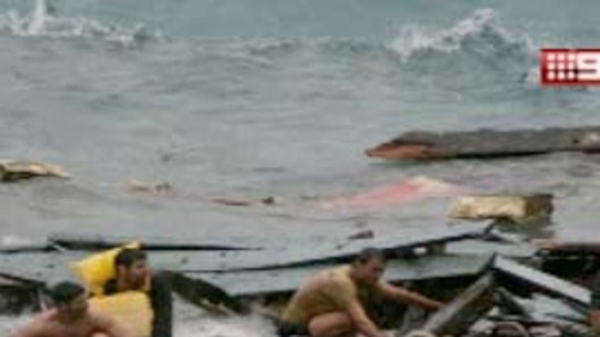 Asylum seekers sit on what remains of their boat.