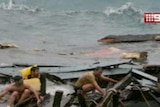 Asylum seekers sit on what remains of their boat.