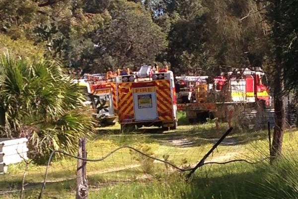 In a rural setting with trees, several fire engines are parked after a man died in a tractor accident at Ballajura