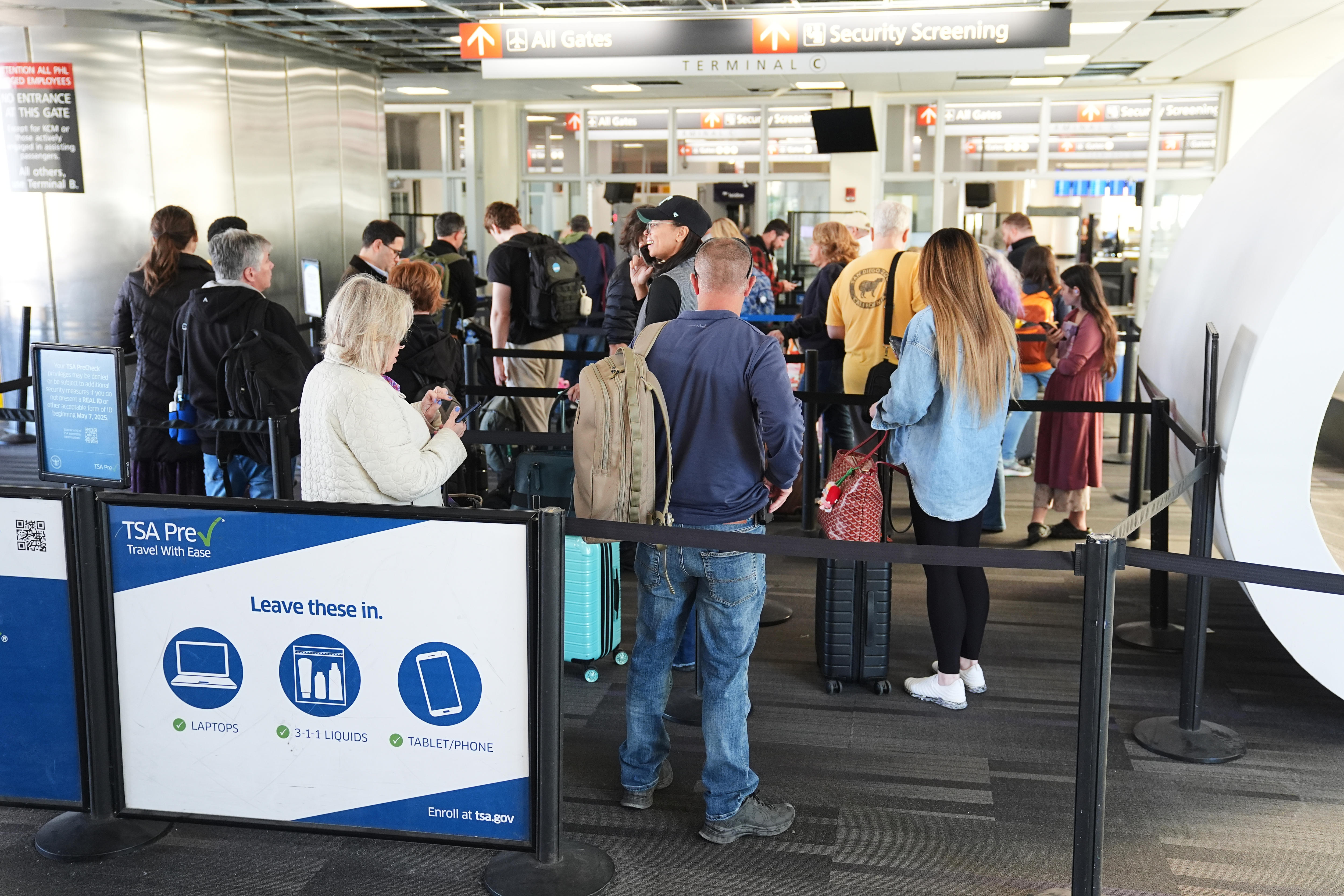 Male and female travellers standing with bags in a US TSA security screening airport line