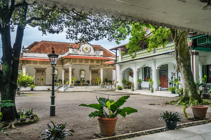 The palace of the Sultan of Yogyakarta stands surrounded by lush, green plants and a bare courtyard.