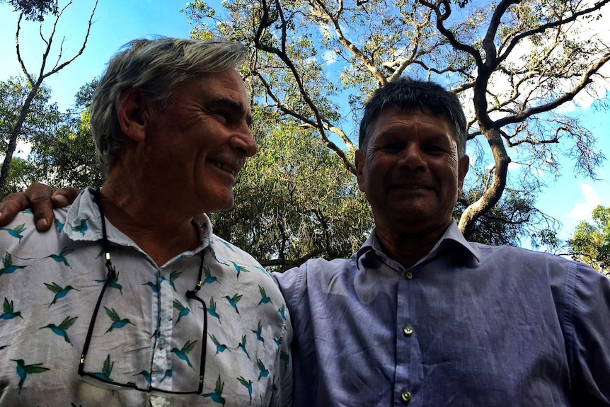 Nigel Jamieson and Noongar elder Dr Richard Walley standing with arms around each other outside under trees