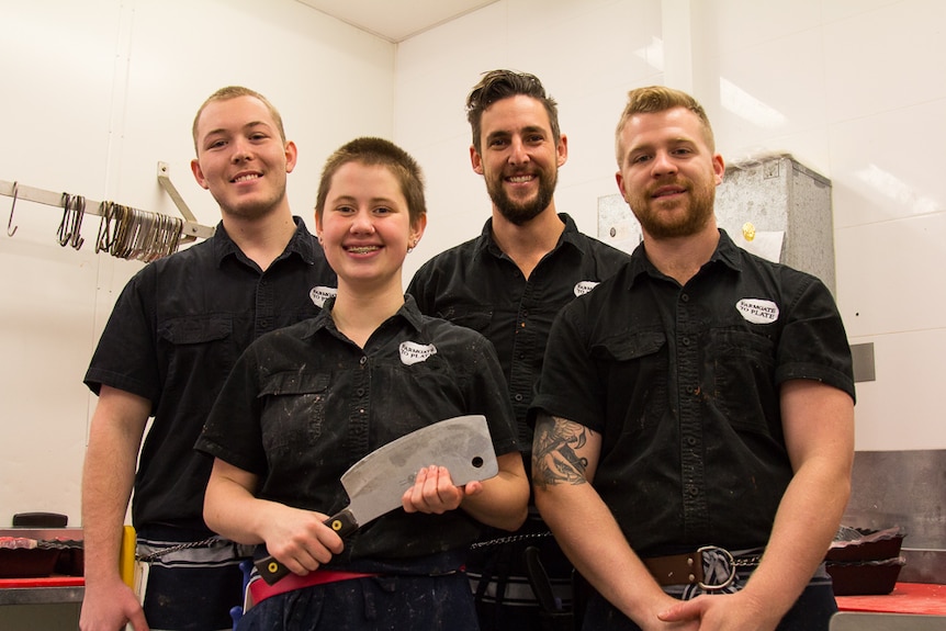 Apprentice butcher Sarah Wadland holding a cleaver and standing next to her male colleagues.