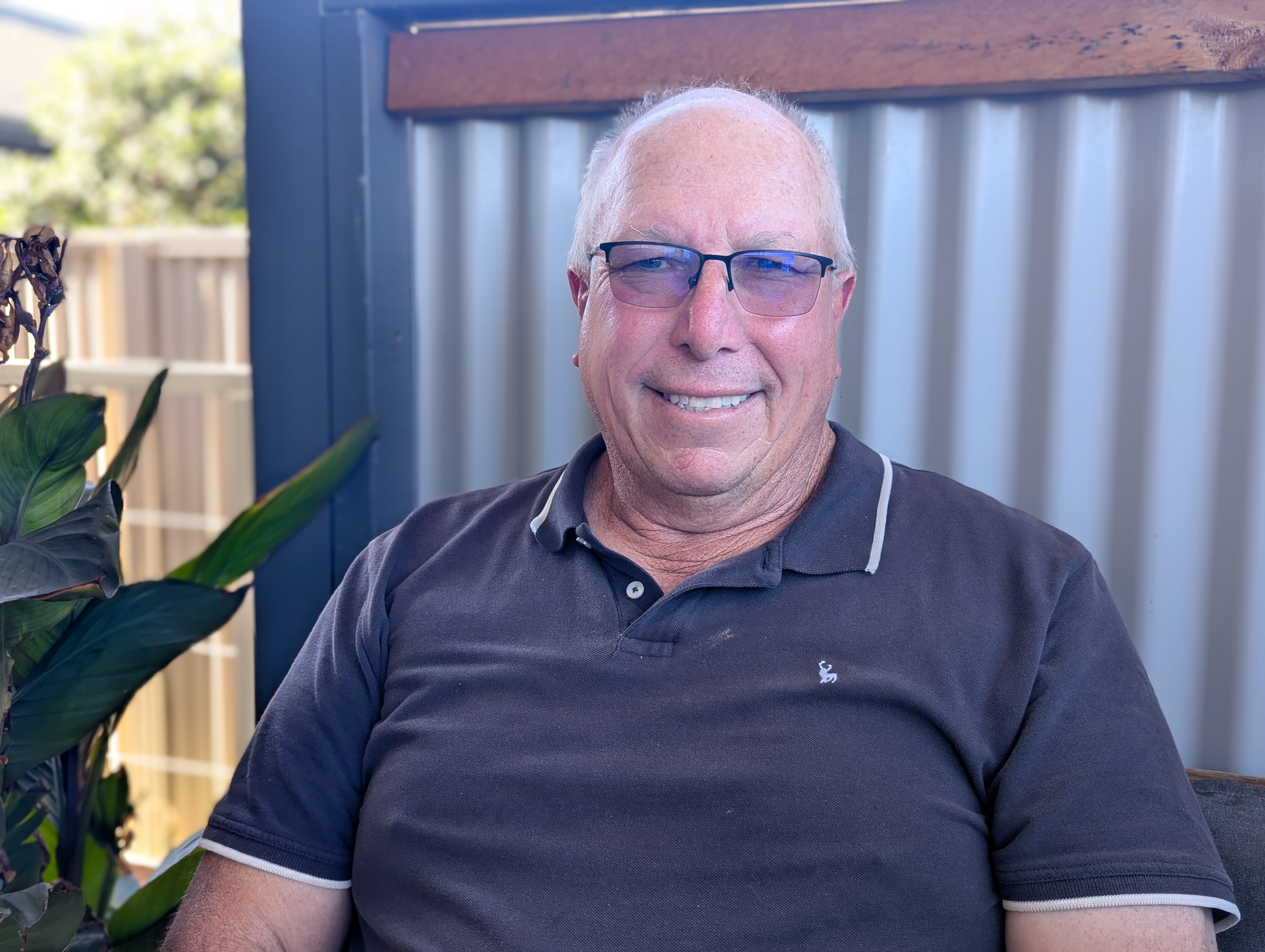 A grey-haired balding fair-skinned bespectacled man, Steve, in grey polo sits.