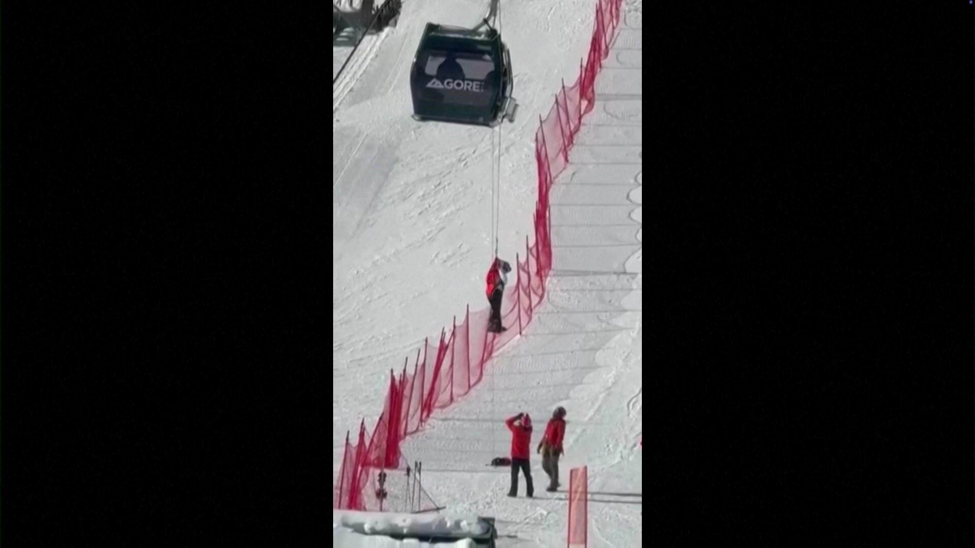 Person dangling on a rope from a gondola at a ski field.