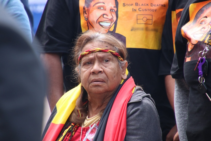 An older lady with a head band with a solemn expression seated at a rally