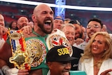 Surrounded by supporters, a boxer roars in triumph as he holds his world title belts in his hands.
