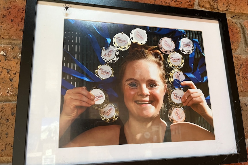 A framed picture of Phoebe Mitchell holding her medals for swimming. 