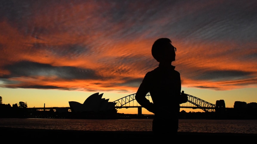 A jogger runs past the Sydney Opera House and Sydney Harbour Bridge at sunset.