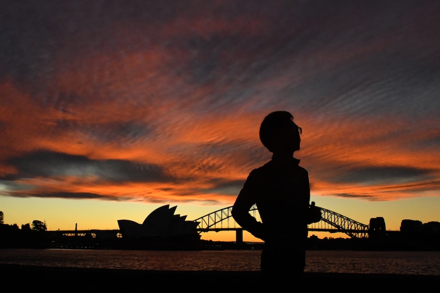 A jogger runs past the Sydney Opera House and Sydney Harbour Bridge at sunset.