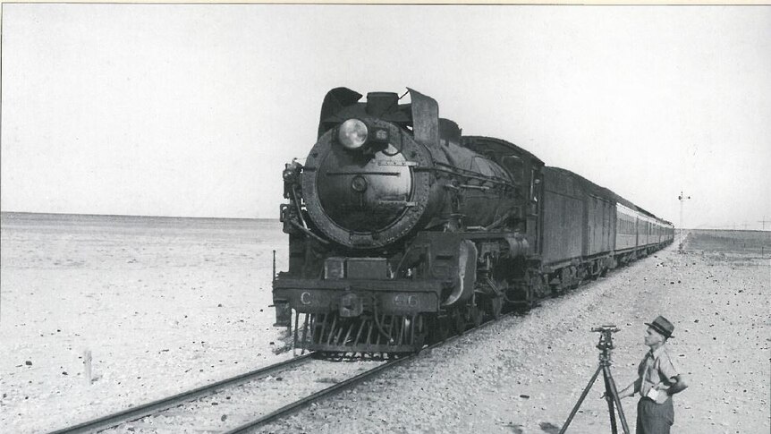 Image of a steam train on the Nullarbor Plain, with a surveyor watching on in the foreground.
