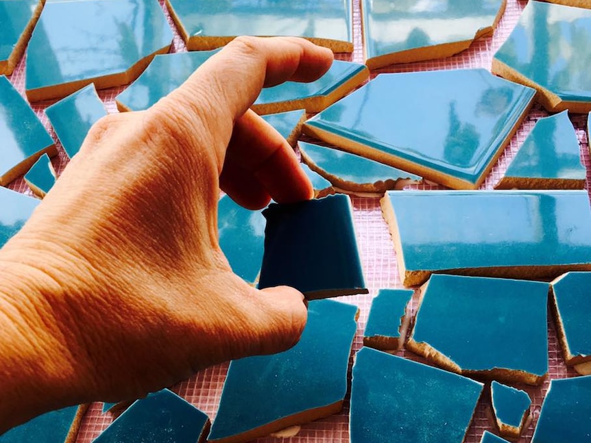 A hand places an irregularly shaped shard of tile into a mosaic