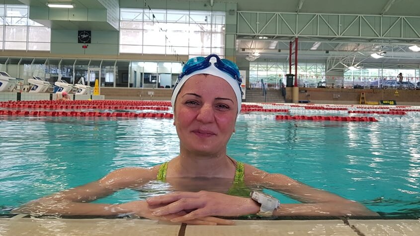 smiling, tired woman in a bathing cap with goggles on her head, in a pool resting her arms on the edge
