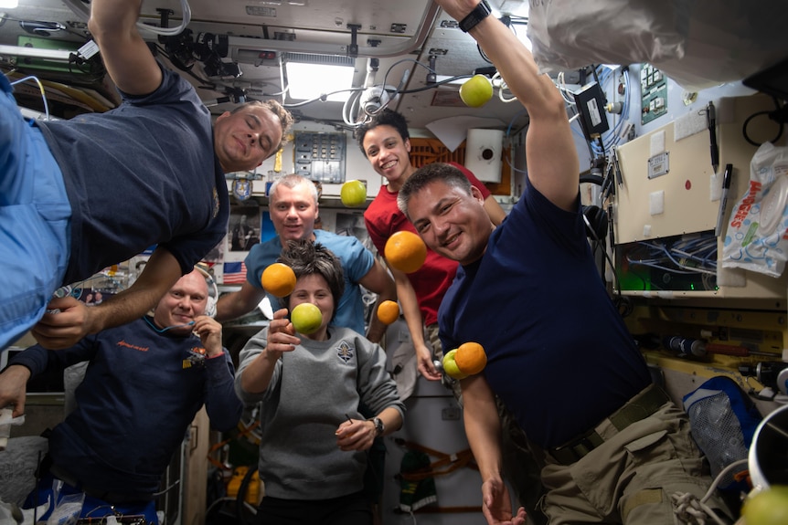 Six astronauts are pictured with fresh fruit flying weightlessly in front of them