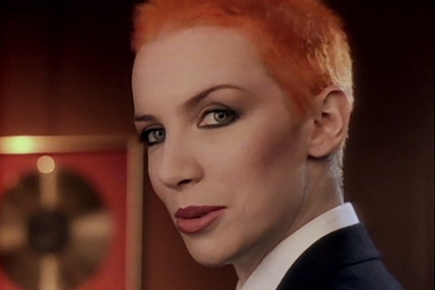A short-haired besuited Annie Lennox smirks at the camera.