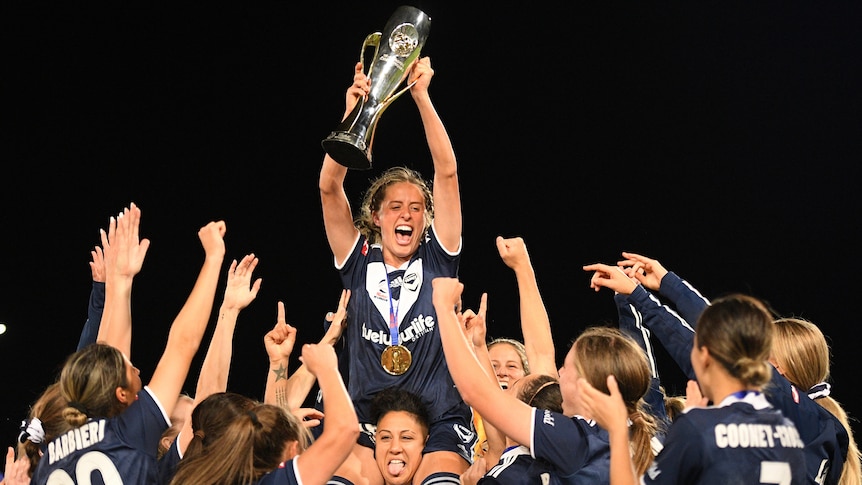 A Melbourne Victory W-League player holds up the trophy above her teammates.