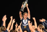 A Melbourne Victory W-League player holds up the trophy above her teammates.