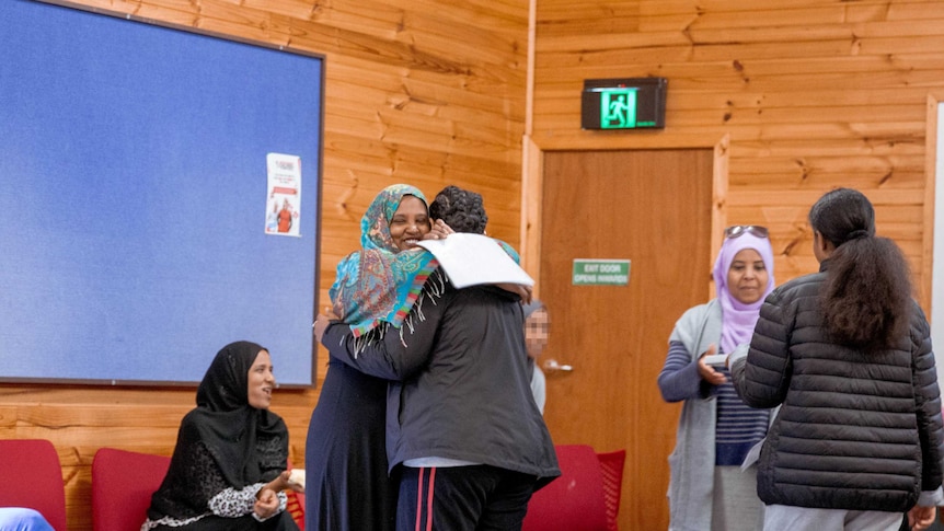 A mother and daughter hug in a workshop.