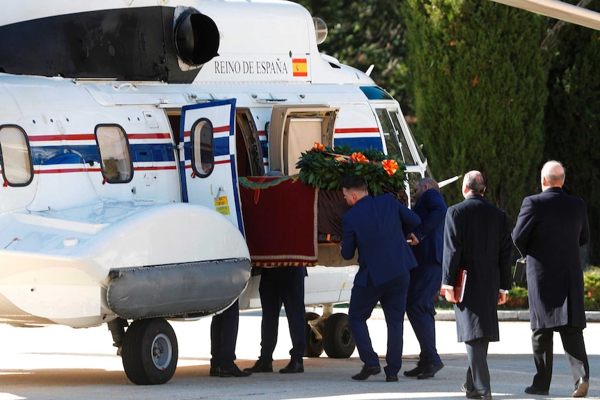 Franco's coffin is slid into a small plane by several men dressed in dark blue