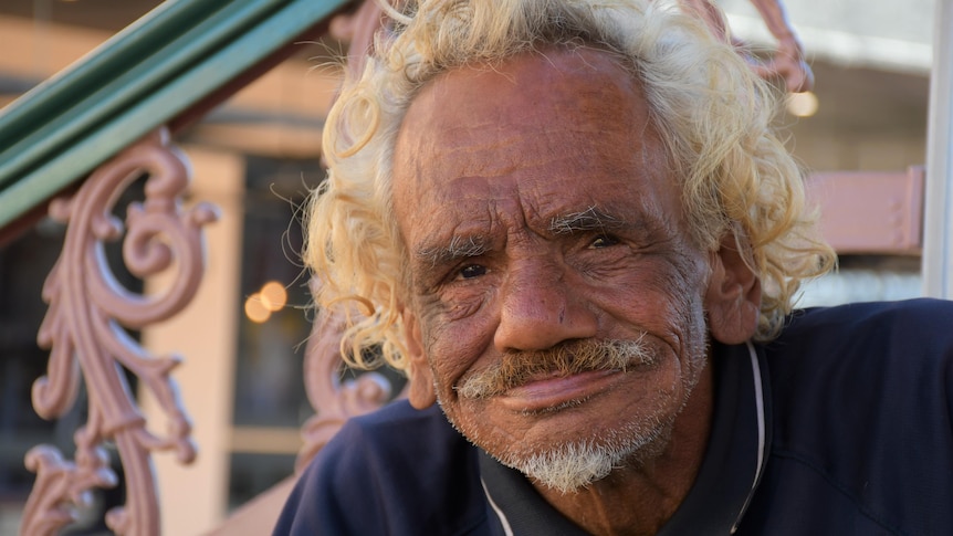 An Aboriginal man with curly blonde hair smiles at the camera.