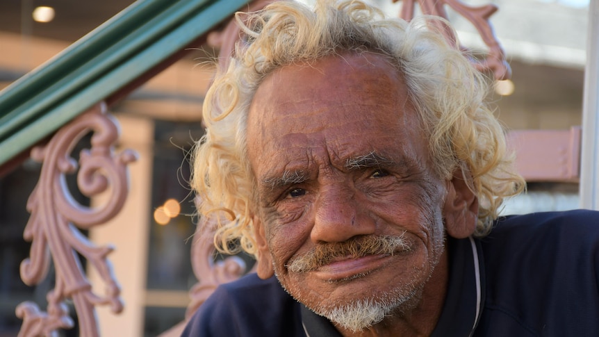 A Aboriginal man with curly blonde hair smiles at the camera.