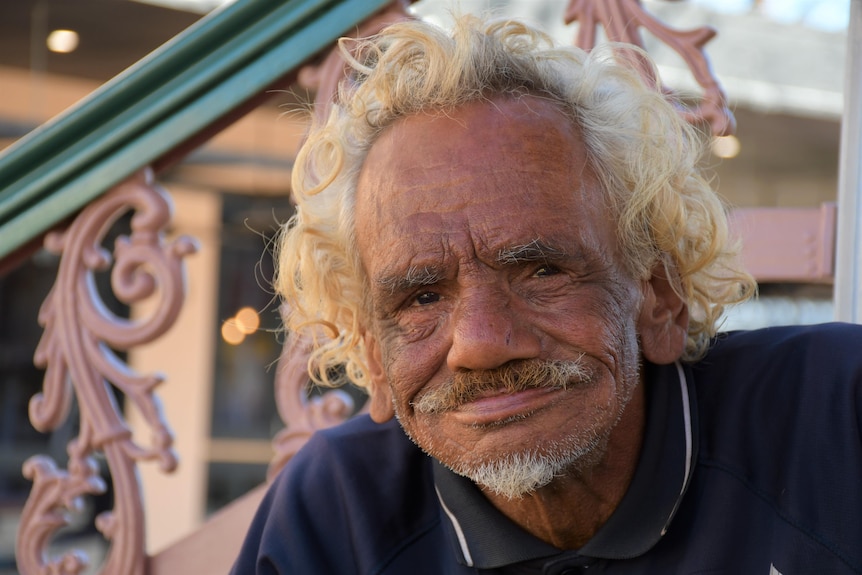 An Aboriginal man with curly blonde hair smiles at the camera.