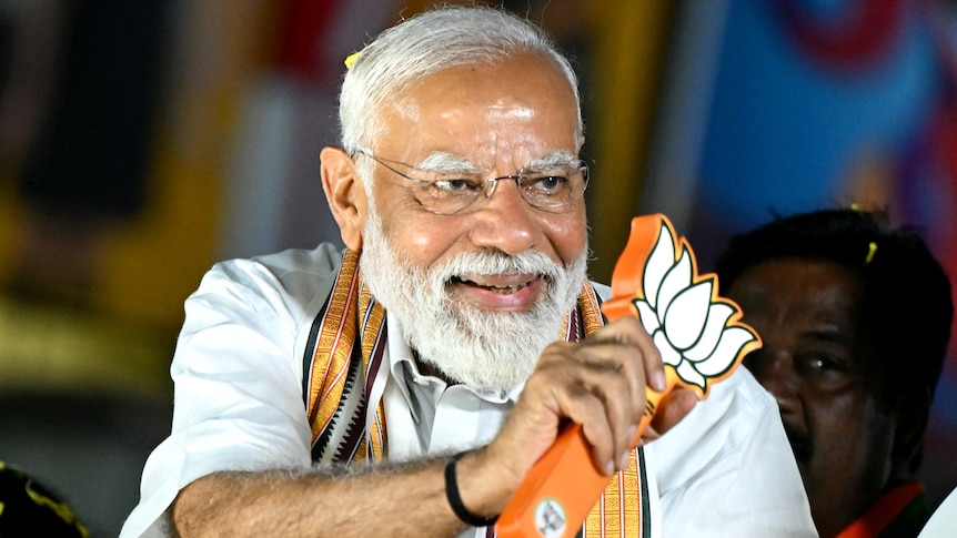 Narendra Modi smiles as he waves a stylised lotus leaf symbol.