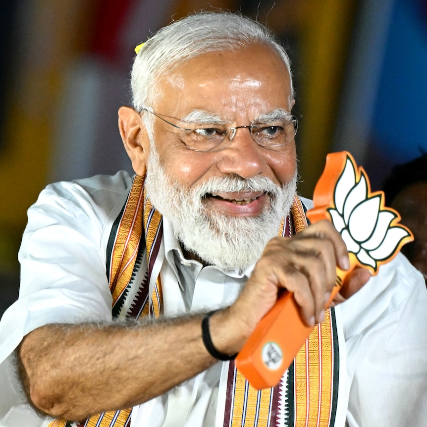 Narendra Modi smiles as he waves a stylised lotus leaf symbol.